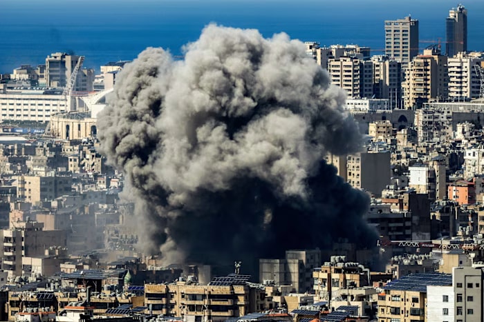 Thick black smoke rises over densely packed buildings in Beirut after an air strike, with the sea visible in the background