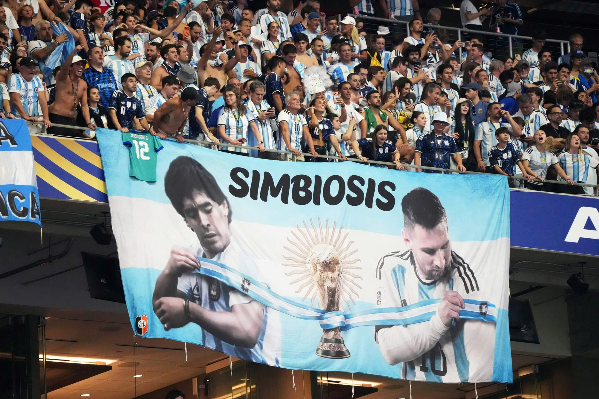 Dòng chữ: symbiosis (sự cộng sinh) trên lá cờ có hình Messi và Maradona, mỗi người chỉ có 1 cúp vô địch. Ảnh: Getty