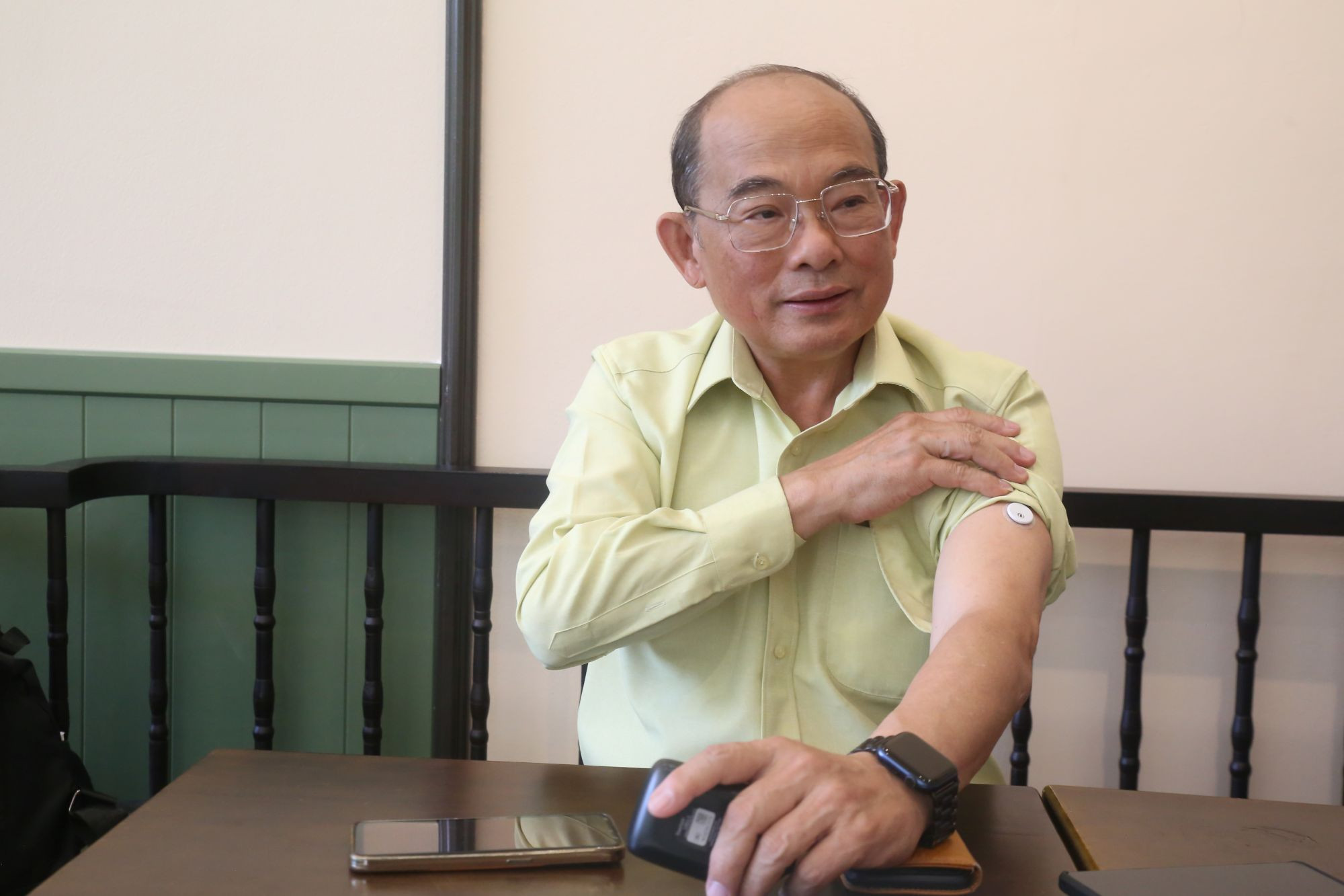 Giáo sư Từ Trung Chấn vén tay áo cho xem con chip cảm ứng đo đường huyết đang được dán trên bắp tay