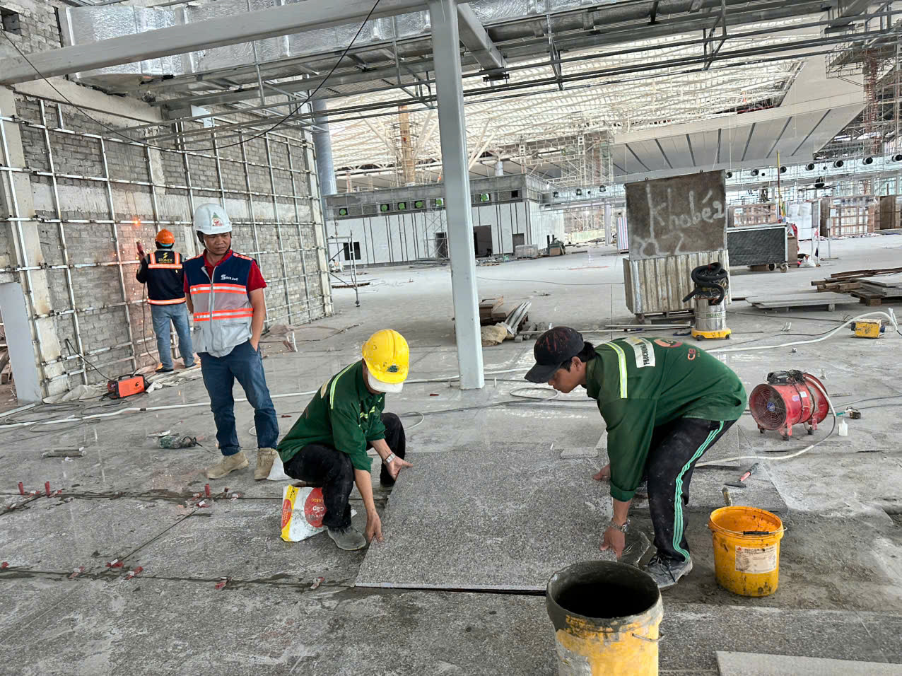 Các công nhân và kỹ sư đang tập trung thi công lát đá đá hoa cương sàn nhà ga hành khách Sân bay quốc tế Long Thành, song song với công tác hàn hoàn thiện các kết cấu tường bên trong.