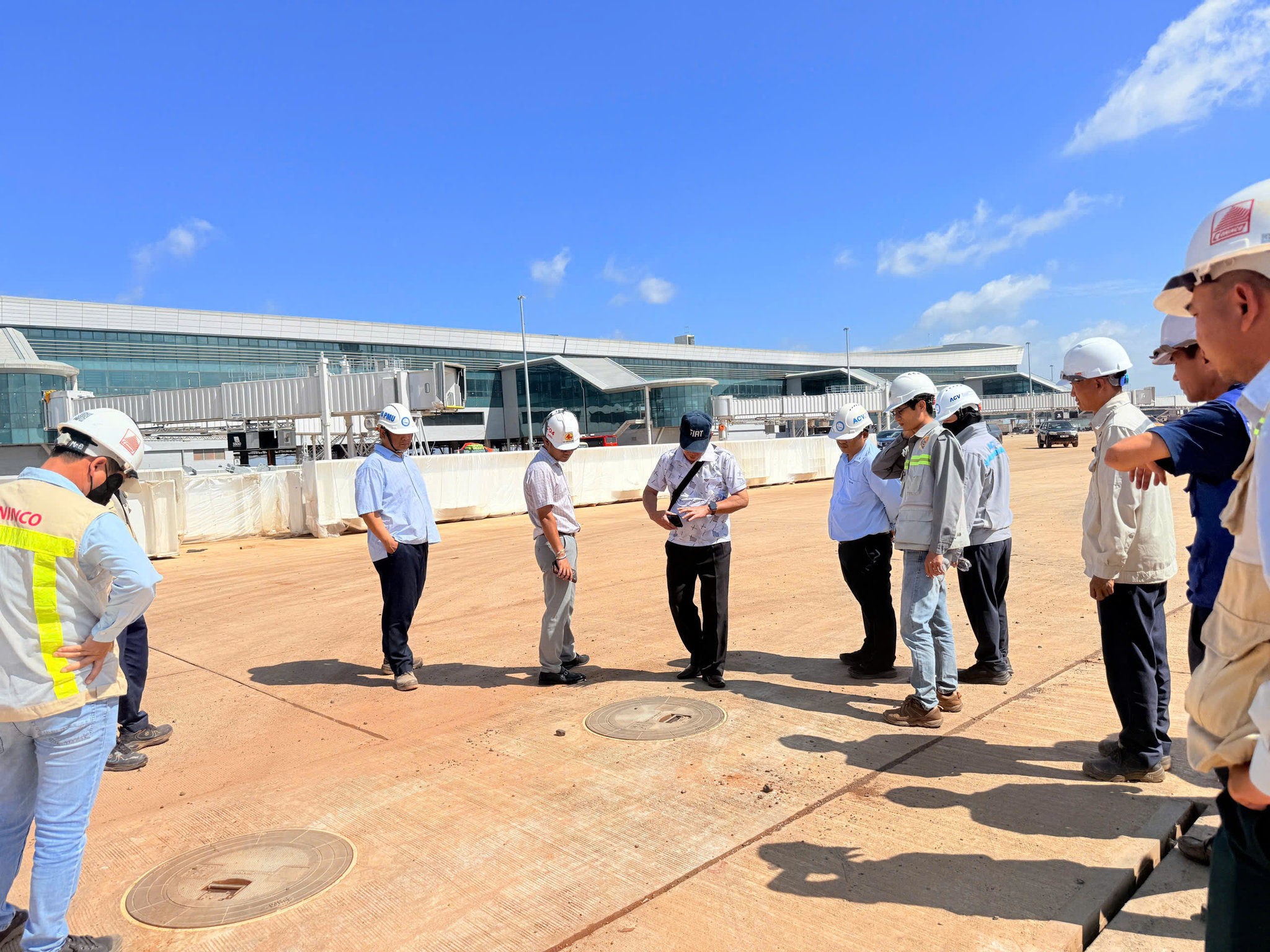 Một nhóm kỹ sư, giám sát viên và công nhân đang kiểm tra thực địa tại khu vực sân bãi của một dự án xây dựng nhà ga sân bay hiện đại