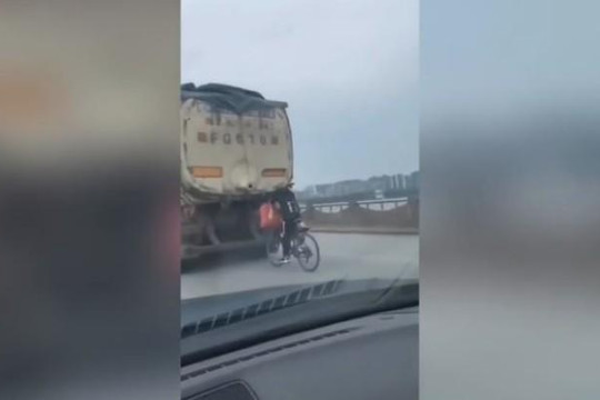 Người đi xe đạp bám vào xe tải đang chạy trên đường để 'đi nhờ'